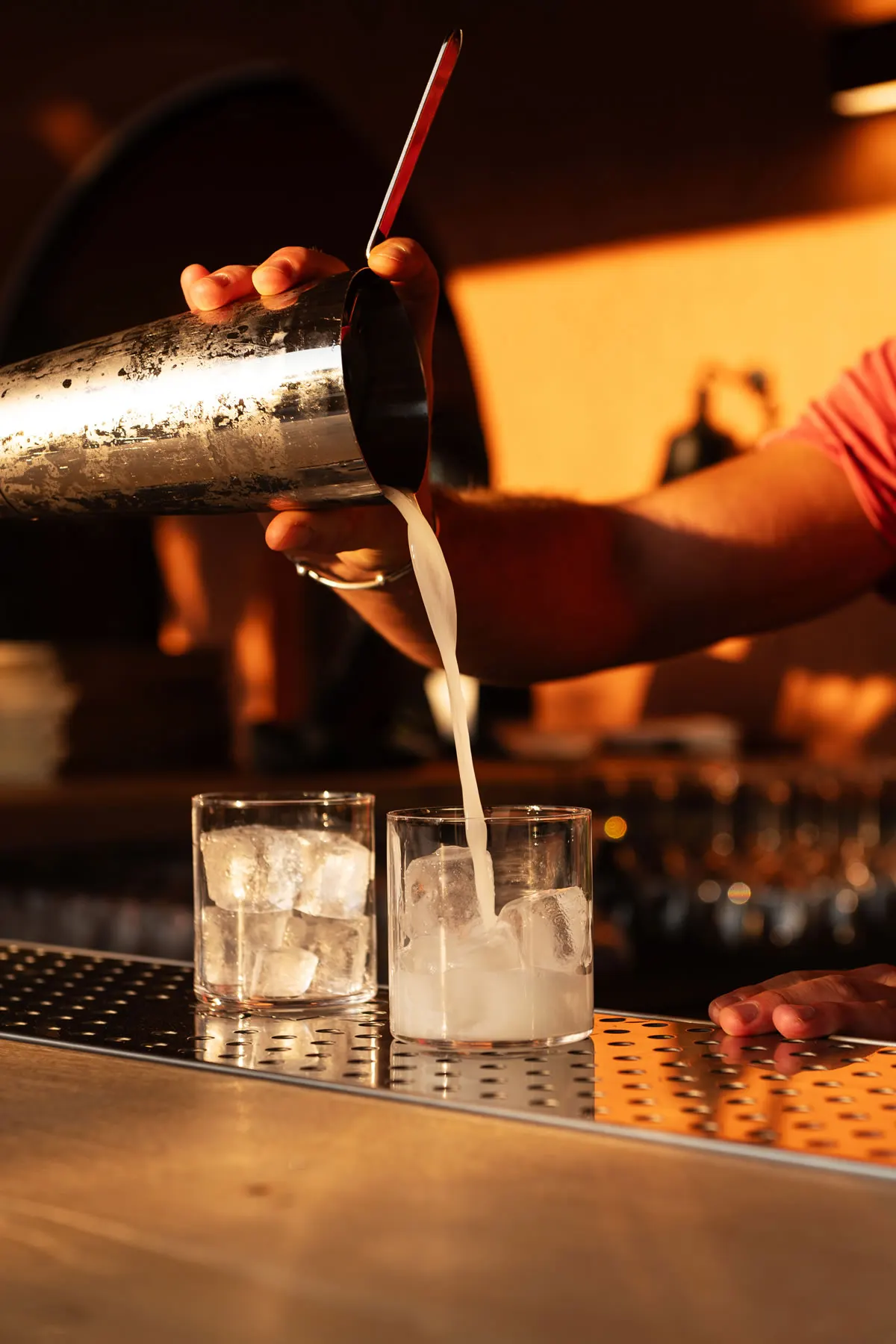 Il bartender di Jaga versa un cocktail dallo shaker nella luce calda del bancone