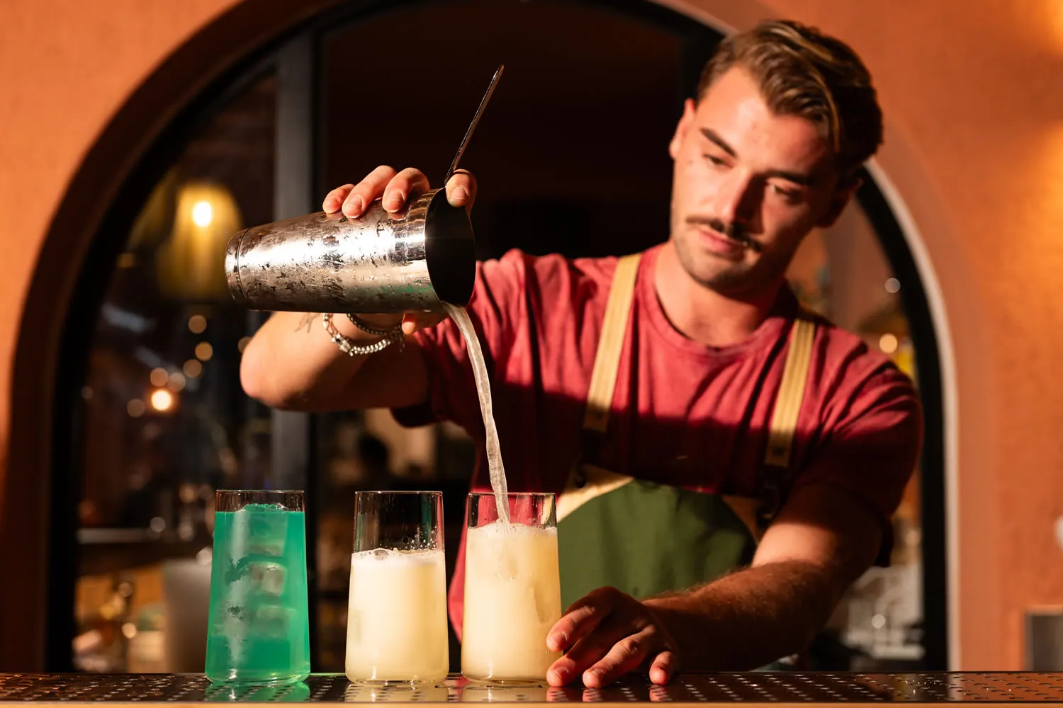 Il bartender al lavoro dietro il bancone, tra bottiglie e luci calde